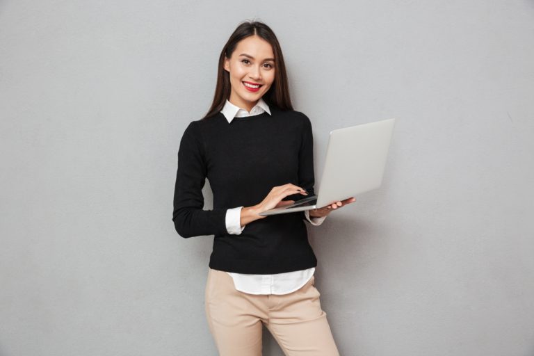 Smiling asian woman in business clothes using laptop computer