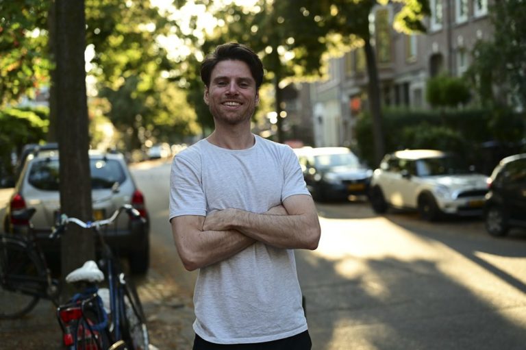 Male master student smiling and standing with his arms crossed i