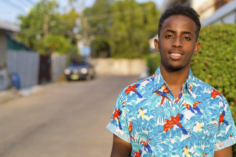 Face of happy young African tourist man smiling outdoors