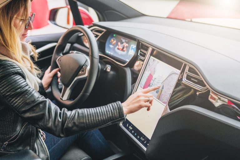 Woman sits behind wheel in car and uses electronic dashboard. Girl traveler looking for way through navigation system.