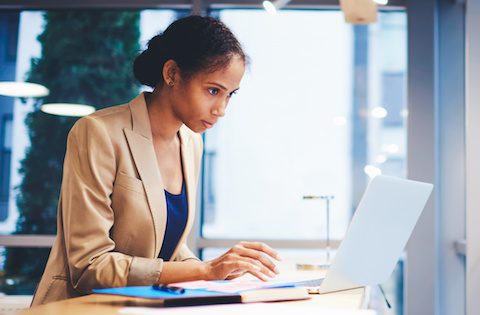 Mindful professional female executive making business report about increasing income and sales of company using data from web site via  modern laptop computer connected to wireless internet in office